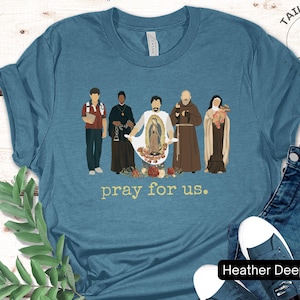 May include: A heather deep teal t-shirt with a graphic of five figures in front of a floral design. The figures are wearing robes and holding religious symbols. The text "pray for us." is printed below the graphic.