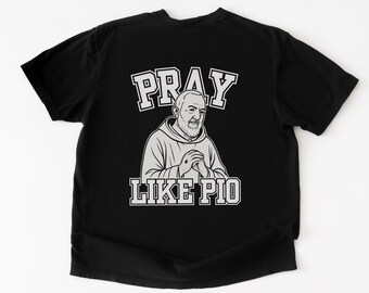 May include: Black t-shirt featuring a graphic of a man in a hooded sweatshirt with the text "PRAY LIKE PIO" in white block letters. The illustration is in a grayscale color scheme.