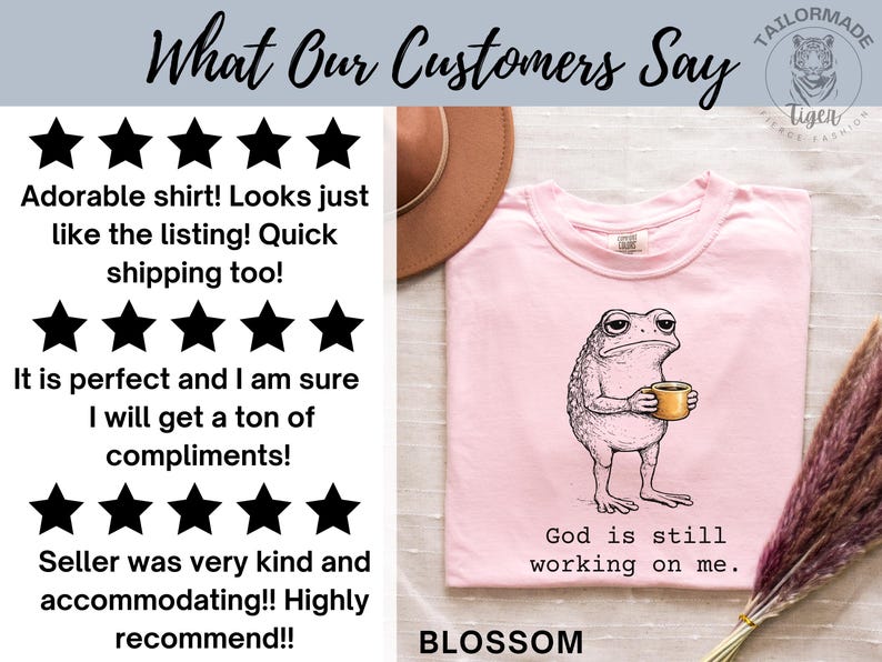 May include: A light pink t-shirt with a graphic of a grumpy frog holding a coffee cup. The text "God is still working on me" is below the frog. The word "BLOSSOM" is at the bottom of the shirt.