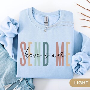 May include: Light blue sweatshirt with the text "SEND ME here i am" in colorful letters.
