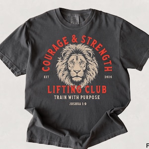 May include: Pepper-colored t-shirt with a distressed graphic. The design features a lion's head within a red circle, with the words "COURAGE & STRENGTH" and "LIFTING CLUB". The text "TRAIN WITH PURPOSE" and "Joshua 1:9" are also included.