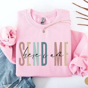May include: Pink sweatshirt with the text "SEND ME here i am" in colorful letters.