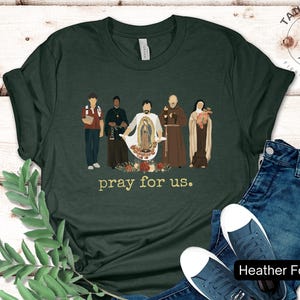 May include: A dark green t-shirt with a graphic of five figures standing in front of a floral design. The text "pray for us." is printed below the graphic.