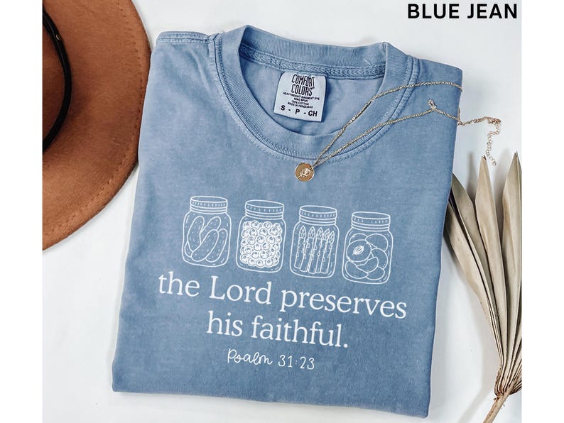 Puede incluir: Una camiseta color azul jean con un gr&aacute;fico blanco de cuatro frascos de vidrio llenos de conservas. Debajo de los frascos, el texto dice: "the Lord preserves his faithful. Psalm 31:23". La camiseta tiene una etiqueta de la marca Comfort Colors.