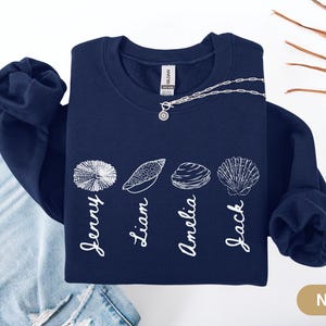 May include: Navy blue sweatshirt with a white design of seashells and names: Jenny, Liam, Amelia, and Jack.