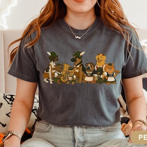 May include: Dark grey t-shirt featuring a cartoon illustration of various dog breeds dressed in traditional Bavarian attire. The dogs are depicted with hats, lederhosen, and instruments, creating a festive and whimsical design. The word "PEPPER" is printed on the bottom right.