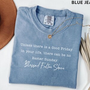 May include: A blue jean coloured t-shirt with the text "Unless there is a Good Friday in your life, there can be no Easter Sunday. Blessed Fulton Sheen." A gold necklace with a pendant is on the shirt.