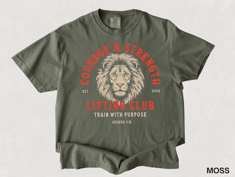 May include: Moss green t-shirt with a lion graphic and the words "COURAGE & STRENGTH" in a red arch. Below the lion is "LIFTING CLUB TRAIN WITH PURPOSE" in red. The text "EST 2026" is also present.