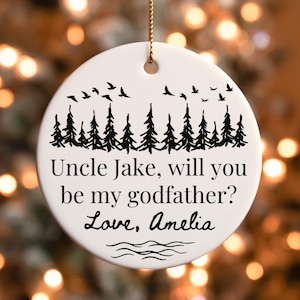 May include: White ceramic Christmas ornament with a black forest and birds design. Text reads "Uncle Jake, will you be my godfather? Love, Amelia." Includes a gold string for hanging.