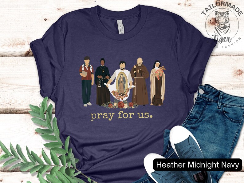 May include: A navy blue t-shirt with a graphic of five figures standing in front of a floral design. The text "pray for us." is printed below the graphic.