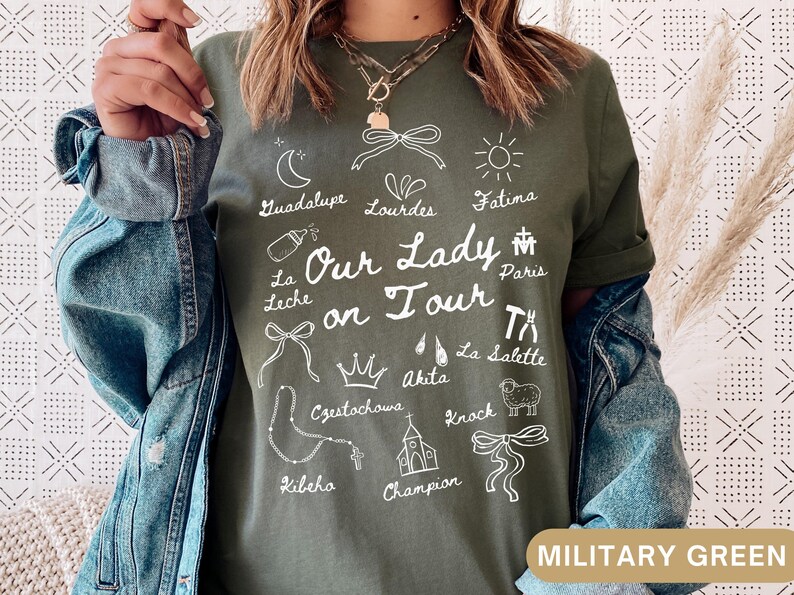 Puede incluir: Una camiseta verde con texto blanco que dice "Nuestra Se&ntilde;ora de gira" y enumera varios lugares, entre ellos Guadalupe, Lourdes, F&aacute;tima, Par&iacute;s, La Leche, Czestochowa, Akita, La Salette, Knock, Kibeho y Champion.