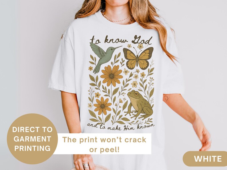 May include: White t-shirt with a nature-themed graphic. The design includes a hummingbird, butterfly, flowers, and a frog, with the text "to know God and to make Him known". The print won't crack or peel.