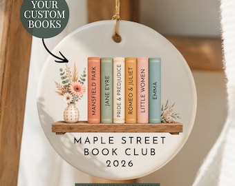 Può includere: Un ornamento rotondo in ceramica bianca con la grafica di uno scaffale in legno che sostiene sei dorsi di libri colorati intitolati Mansfield Park, Jane Eyre, Pride & Prejudice, Romeo & Juliet, Little Women ed Emma, accanto a un vaso di fiori.