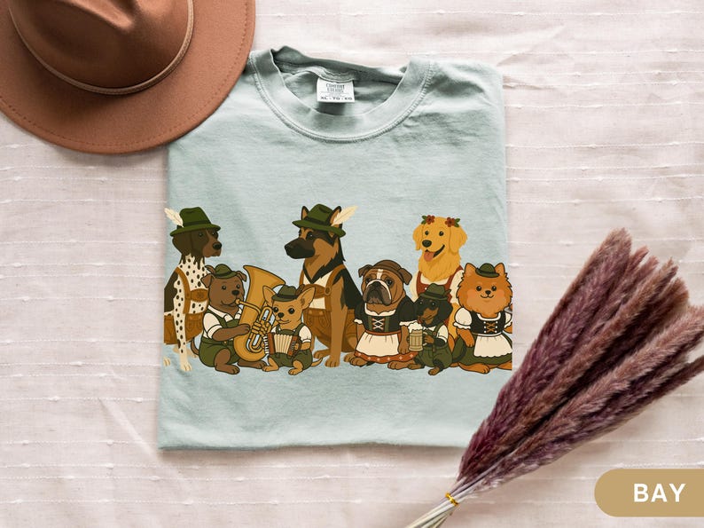 May include: A light blue t-shirt featuring a group of cartoon dogs dressed in traditional Bavarian outfits. The dogs include a Dalmatian, German Shepherd, Bulldog, Golden Retriever, and Pomeranian. Some dogs are playing instruments.