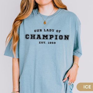 Peut inclure: Un t-shirt bleu clair avec le texte "Our Lady of Champion Est. 1859" imprimé sur le devant.