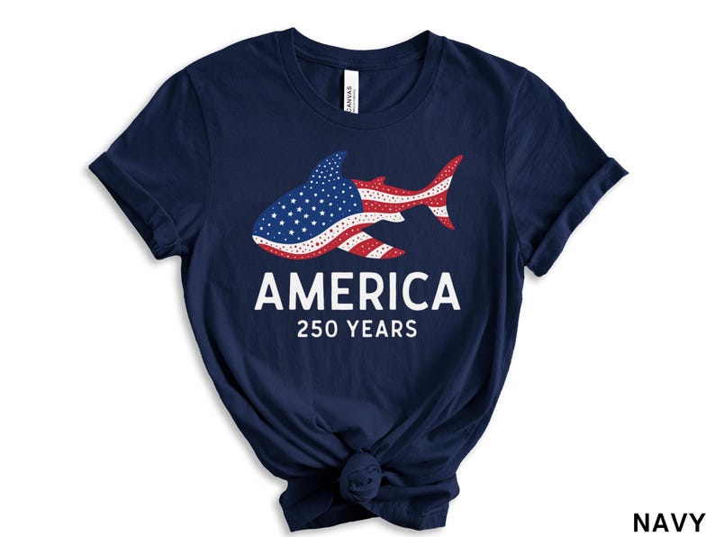 Puede incluir: Camiseta azul marino con un dise&ntilde;o de tibur&oacute;n que incorpora la bandera estadounidense. El texto dice "AMERICA" y "250 YEARS" en blanco. Una camiseta de tem&aacute;tica patri&oacute;tica.