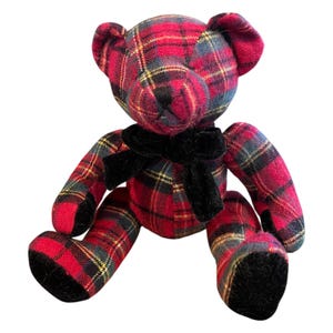 Può includere: Un orsacchiotto di peluche realizzato in tessuto a quadri rosso, nero e giallo. L'orso presenta un nastro di velluto nero legato al collo, dettagli del naso e della bocca cuciti in nero e tessuto di velluto nero sulle piante dei piedi.