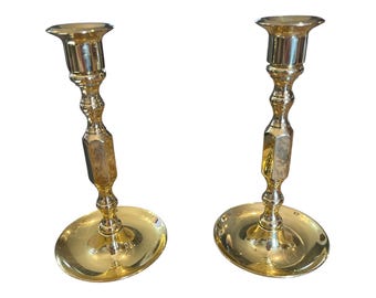 Puede incluir: Un par de candelabros de metal dorado con un diseño simple y elegante. Cada candelabro tiene una base redonda y un tallo alto y delgado con una sección octogonal decorativa.