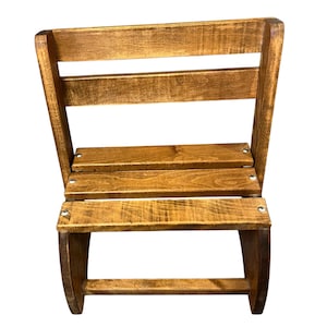 May include: A small, rustic wooden chair with a slatted back and seat. The chair is constructed from stained wood, showcasing the natural grain. The curved legs and back add a touch of elegance to the simple design. The chair is suitable for indoor or outdoor use.