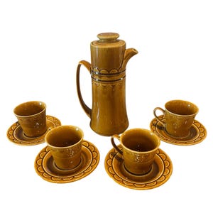 Op de afbeelding: Een vintage bruine keramische koffieset. De set bevat een hoge koffiepot met deksel, vier kopjes en vier schoteltjes. De kopjes en schoteltjes hebben een geschulpte rand. De koffiepot heeft een handvat en een tuit.