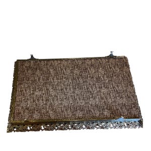 Pode incluir: Bandeja de vaidade retangular vintage com uma inser&ccedil;&atilde;o de tecido castanho e bege texturizado. A bandeja tem uma moldura de metal dourado decorativa com detalhes ornamentados ao longo das bordas e pequenos detalhes decorativos nos cantos.