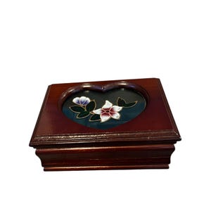 May include: A white ceramic mug with a black handle and the text "But First, Coffee" in a bold, black font. The mug is set against a blurred background, suggesting a cozy setting. The mug appears to be approximately 4 inches tall.