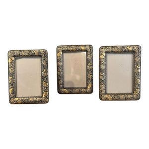 May include: Three rectangular picture frames with a metallic gold finish. Each frame features a raised relief border decorated with detailed carvings of various fruits, including pears and grapes, surrounded by textured leaves and vines.