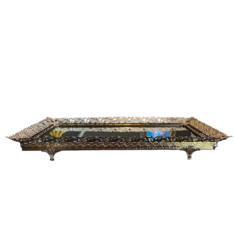 Pode incluir: Uma bandeja retangular dourada e ornamentada com espelho e detalhes intrincados de filigrana nas bordas. A bandeja tem pequenos p&eacute;s decorativos e uma superf&iacute;cie reflexiva. O design &eacute; de inspira&ccedil;&atilde;o vintage.