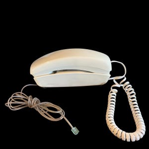 May include: A white landline telephone with a smooth, curved handset resting on a base unit. The device features a coiled white cord connecting the handset to the base and a separate, longer, thin, translucent cord with a clear plastic modular connector.