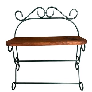 May include: A decorative wall shelf with a dark green metal frame and a wooden shelf. The frame has a scrolled design at the top and curved accents. The shelf is made of dark brown wood.