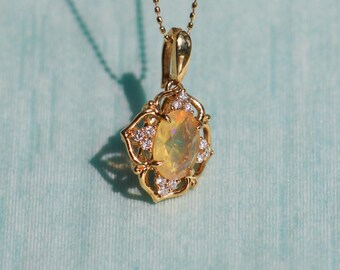 May include: A gold pendant necklace featuring an oval, yellow gemstone surrounded by small, clear gemstones. The pendant is suspended from a delicate gold chain. The text "AFRA JEWELRY STUDIO" is at the bottom of the image.