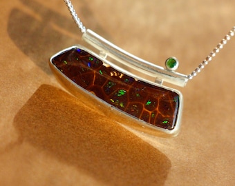 May include: A silver necklace with a brown and green opal pendant and a small green gemstone accent. The pendant is set in a silver frame and hangs from a delicate silver chain.