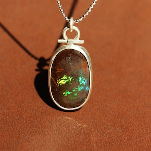 May include: A silver chain necklace with a silver pendant featuring a brown oval opal with green and yellow iridescent flashes.