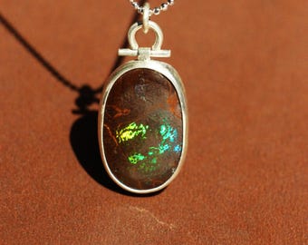 May include: A silver chain necklace with a silver pendant featuring a brown oval opal with green and yellow iridescent flashes.