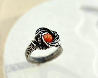 May include: A silver wire wrapped ring with an orange gemstone in the center.