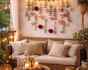 May include: A cozy outdoor living space with a woven sofa, pillows, and a round coffee table. A floral wall hanging with string lights and candles creates a warm, inviting atmosphere. Decorative lanterns and hanging plants add to the ambiance.