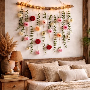May include: A floral wall hanging with a rustic wooden branch adorned with string lights. The arrangement features hanging vines with pink, red, and white flowers, creating a bohemian bedroom decor.