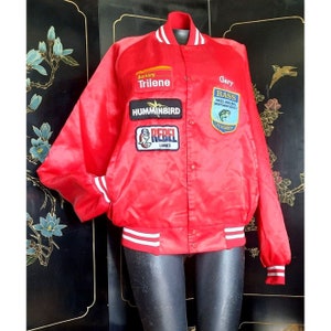 May include: Red satin bomber jacket with white and red striped cuffs and collar. The jacket has several patches, including "Berkeley Trilene", "Humminbird", "Rebel Lures", and "Bass Anglers Sportsman Society Life Member".