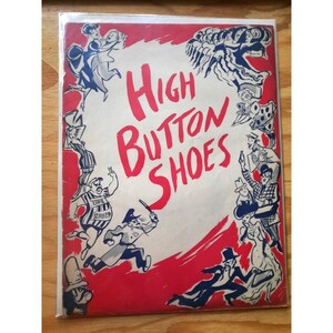 Puede incluir: Una portada de libro vintage con una ilustración roja, blanca y azul de personas que llevan zapatos de botón alto. El título del libro es "High Button Shoes".