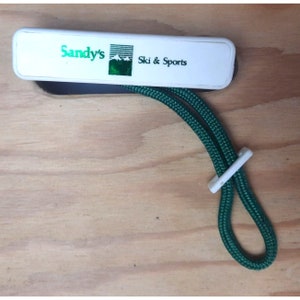 May include: White plastic key chain with a green logo that says "Sandy's Ski & Sports". The key chain has a green cord.