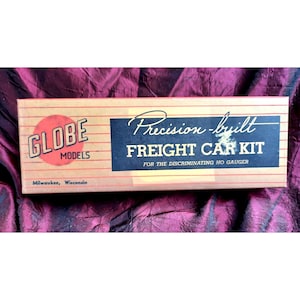 May include: A brown cardboard box with red and white stripes. The box has the text "GLOBE MODELS" in a red circle and the text "Precision-built FREIGHT CAR KIT FOR THE DISCRIMINATING HO GAUGER" in black.