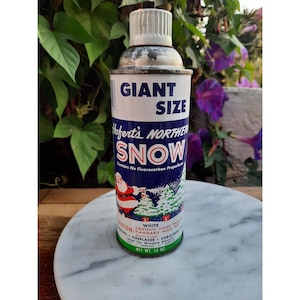 May include: A vintage can of Hofert's Northern Snow, a white artificial snow product in a giant size can. The can features a blue and white label with a Santa Claus illustration and the text "GIANT SIZE Hofert's NORTHERN SNOW Contains No Fluorocarbon Propellant". The can is 13 ounces.