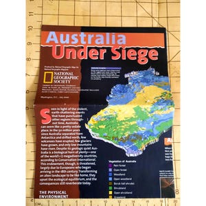 Könnte beinhalten: Eine Karte von Australien mit dem Titel "Australien unter Belagerung" aus der Juli-Ausgabe 2000 des National Geographic Magazins. Die Karte zeigt die verschiedenen Vegetationstypen in Australien, darunter Regenwald, offener Wald, Wald, offener Wald, Gestrüpp, Buschland, offenes Buschland und Grasland.