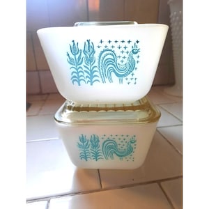 Puede incluir: Dos platos para hornear de cerámica blanca con un diseño de gallo y maíz azul y blanco. Los platos están apilados uno encima del otro.