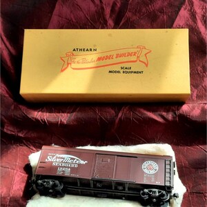 May include: A brown model train boxcar with the words "Silver Meteor" and "Seaboard" printed on the side. The boxcar is on a white surface and has a red and white Seaboard Railroad logo on the side.