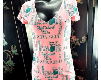 May include: Pink t-shirt with a repeated pattern of the text "Paul Frank" in a green and white font.