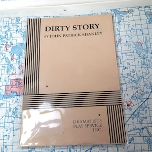 May include: A tan-colored play script cover with black stripes and a star on the top right corner. The title "DIRTY STORY" is printed in black letters, followed by "BY JOHN PATRICK SHANLEY" in smaller letters. The bottom right corner has the text "DRAMATISTS PLAY SERVICE INC."