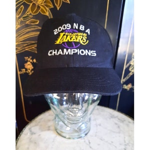 May include: A black baseball cap with the Los Angeles Lakers logo and the text "2009 NBA CHAMPIONS" embroidered on the front.