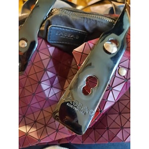 May include: A black and silver geometric handbag with a black leather strap. The strap has a silver buckle and the bag has the text "BAO BAO ISSEY MIYAKE" on it.