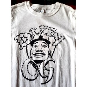 May include: White t-shirt with a black and white graphic print of a person with a marijuana leaf on their hat. The graphic also includes the text "Dizzy OG".